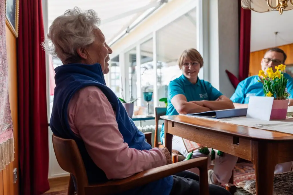 Seniorin am Esstisch, im Hintergrund eine Pflegekraft der Diakoniestation Pforzheim