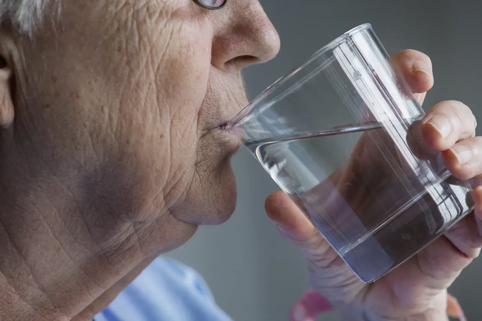 Ältere Frau trinkt aus einem Glas Wasser, ausreichendes Trinken entlastet die Blase
