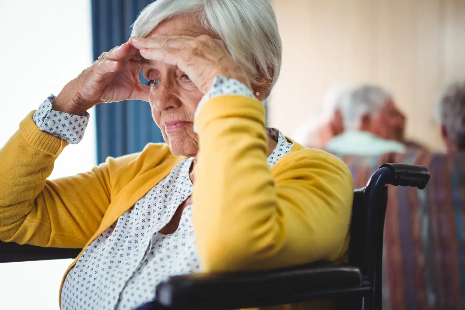 Verwirrte Seniorin im Rollstuhl fasst sich an die Stirn, erste Anzeichen einer Demenz erkennen
