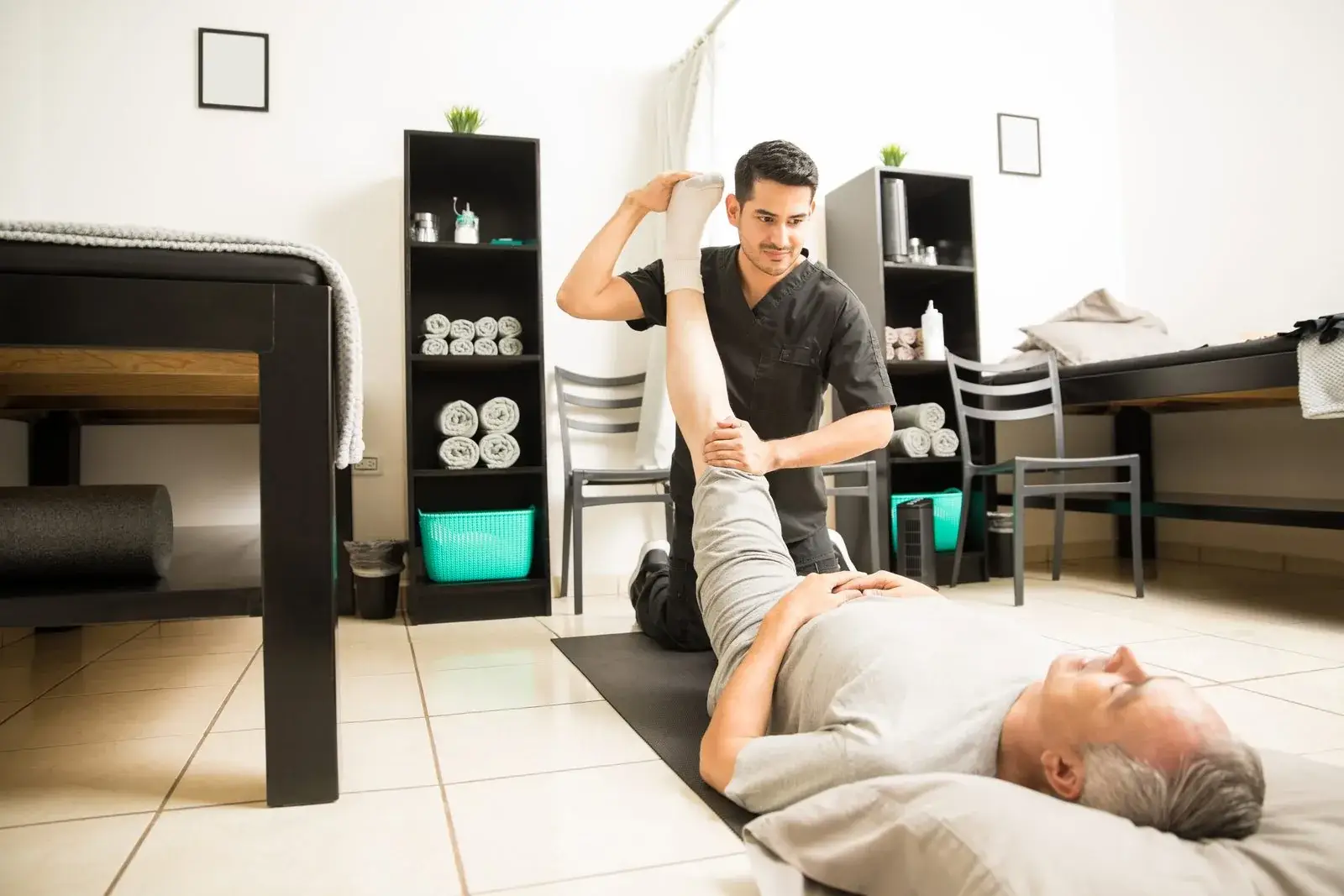 Therapeut bewegt das Bein eines liegenden älteren Mannes in Hüfte und Knie durch