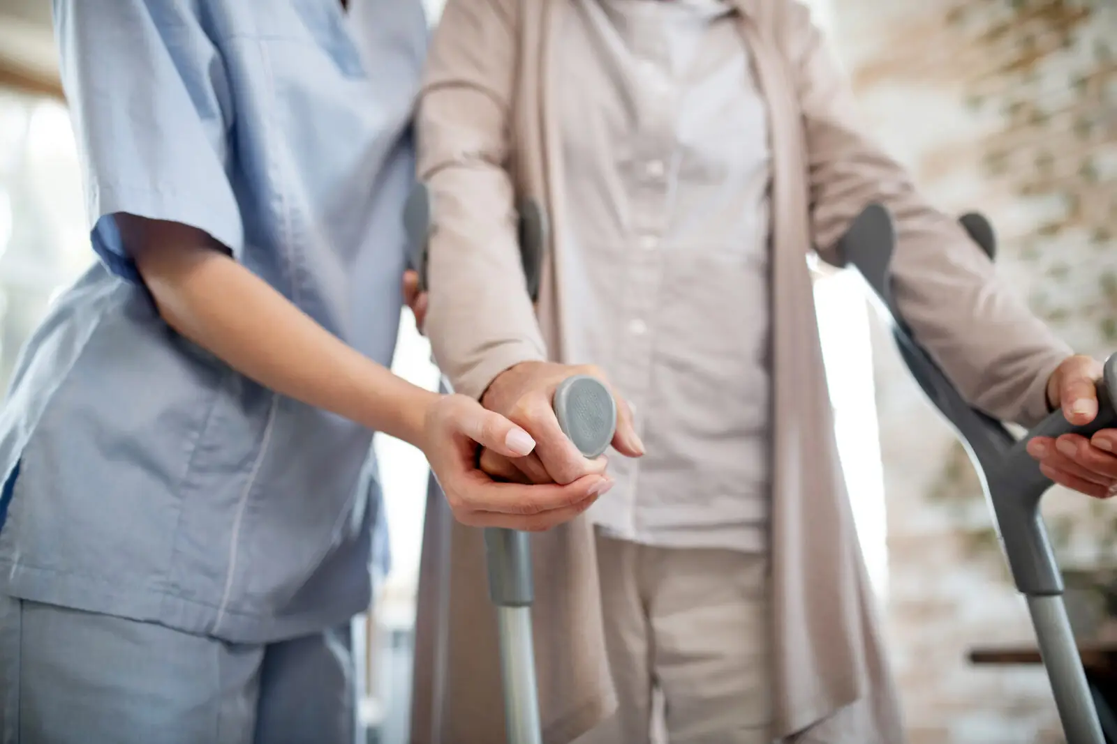 Pflegerin unterstützt Seniorin mit Gehhilfen, körperbezogene Pflege als Pflegesachleistung