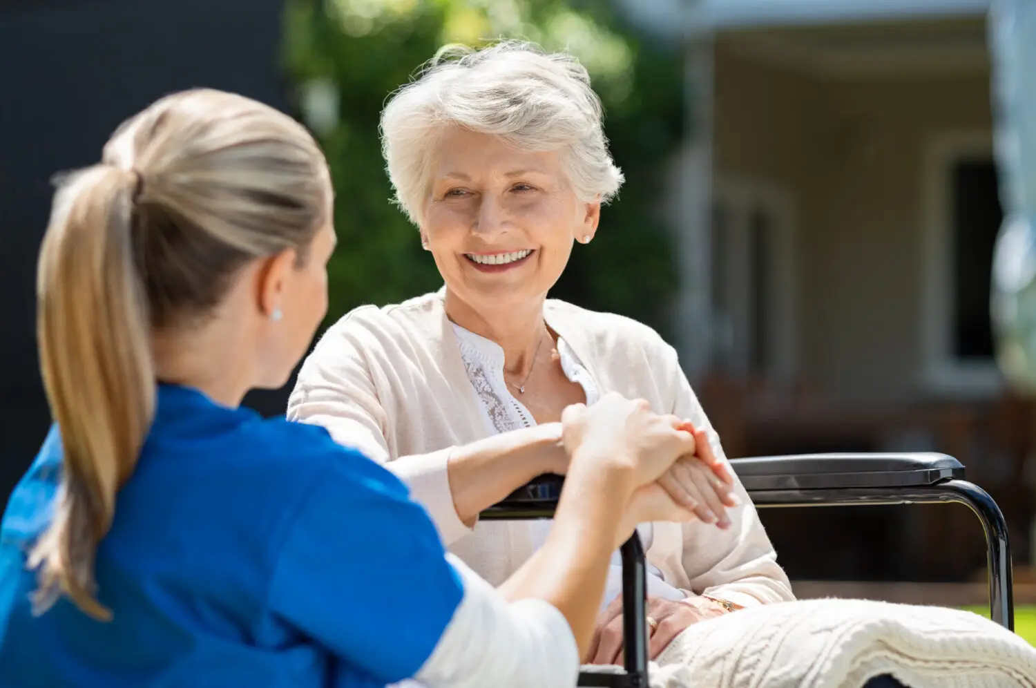 Pflegefachkraft eines ambulanten Pflegedienstes betreut lächelnde Seniorin im Rollstuhl, Pflegesachleistungen im Alltag