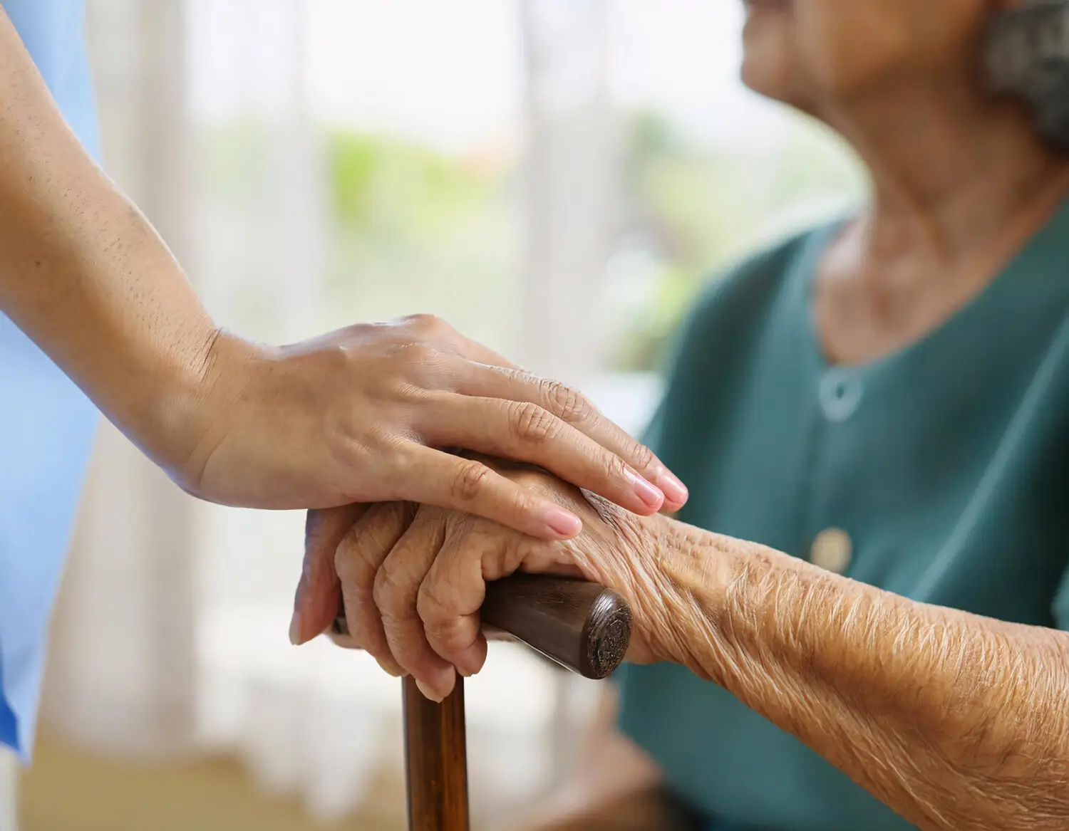 Pflegekraft hält die Hand einer Seniorin mit Gehstock bei Schmerzen im Alter