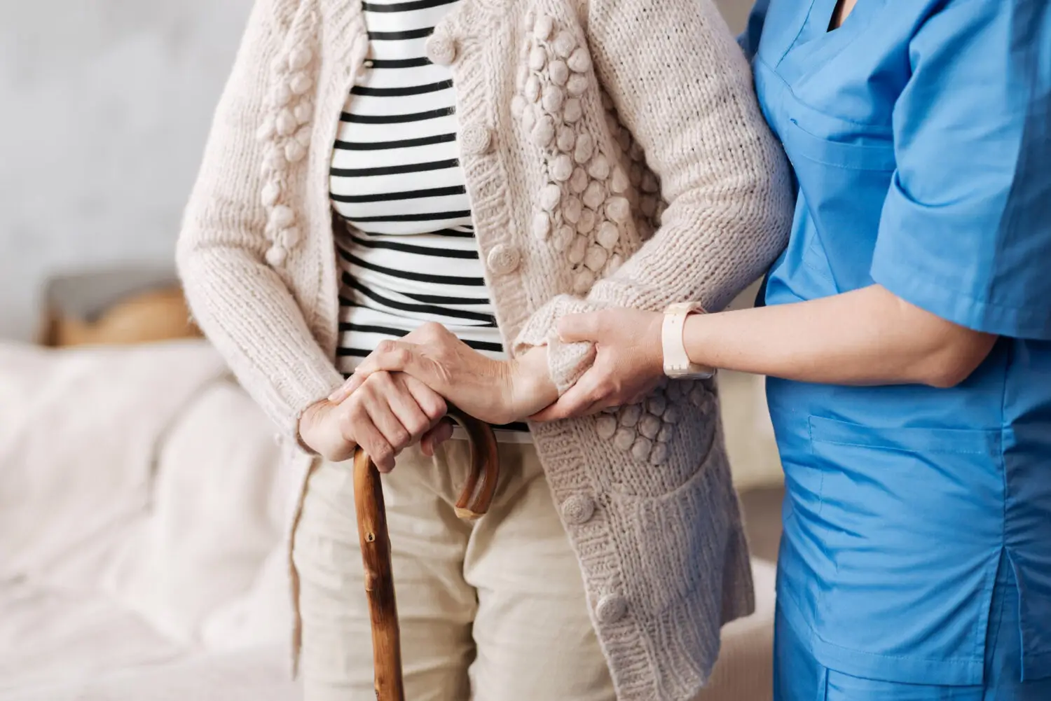Pflegerin stützt Seniorin mit Gehstock beim Gehen trotz Gelenkschmerzen im Alter