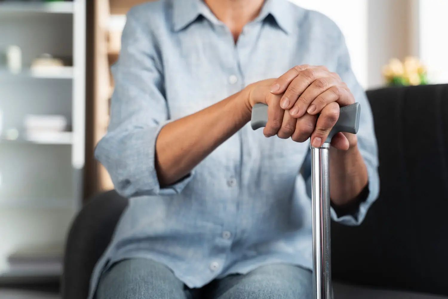 Senior stützt beide Hände auf einen Gehstock, Gehhilfen zur Sturzprophylaxe im Alter