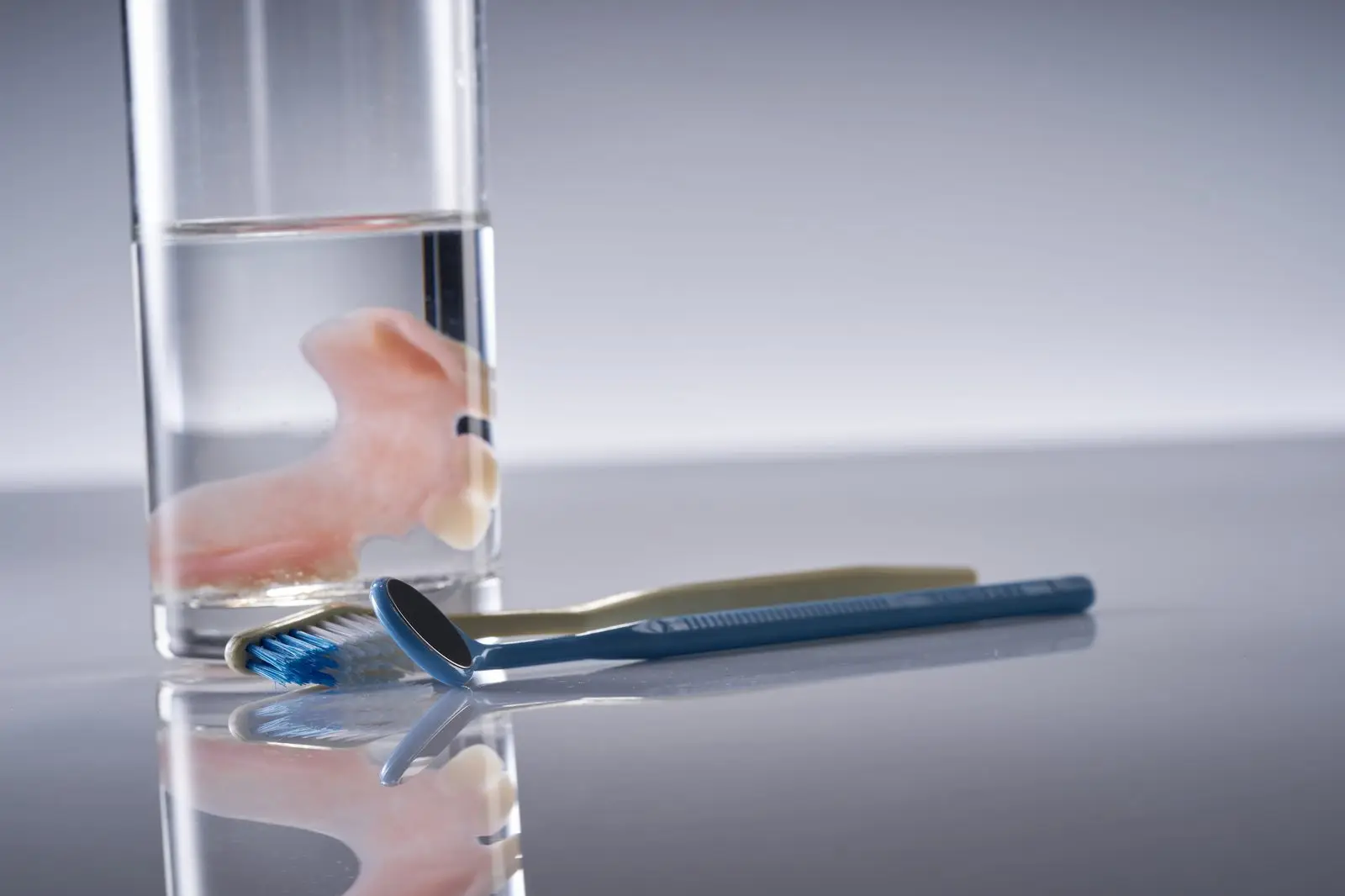 Zahnprothese im Wasserglas neben Zahnbürste und Handspiegel auf der Ablage